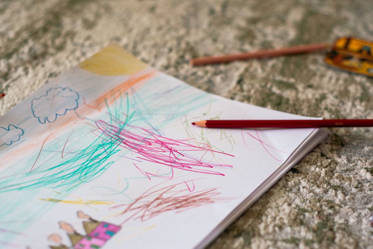 A vibrant child's drawing on paper with colored pencils scattered on a carpet.