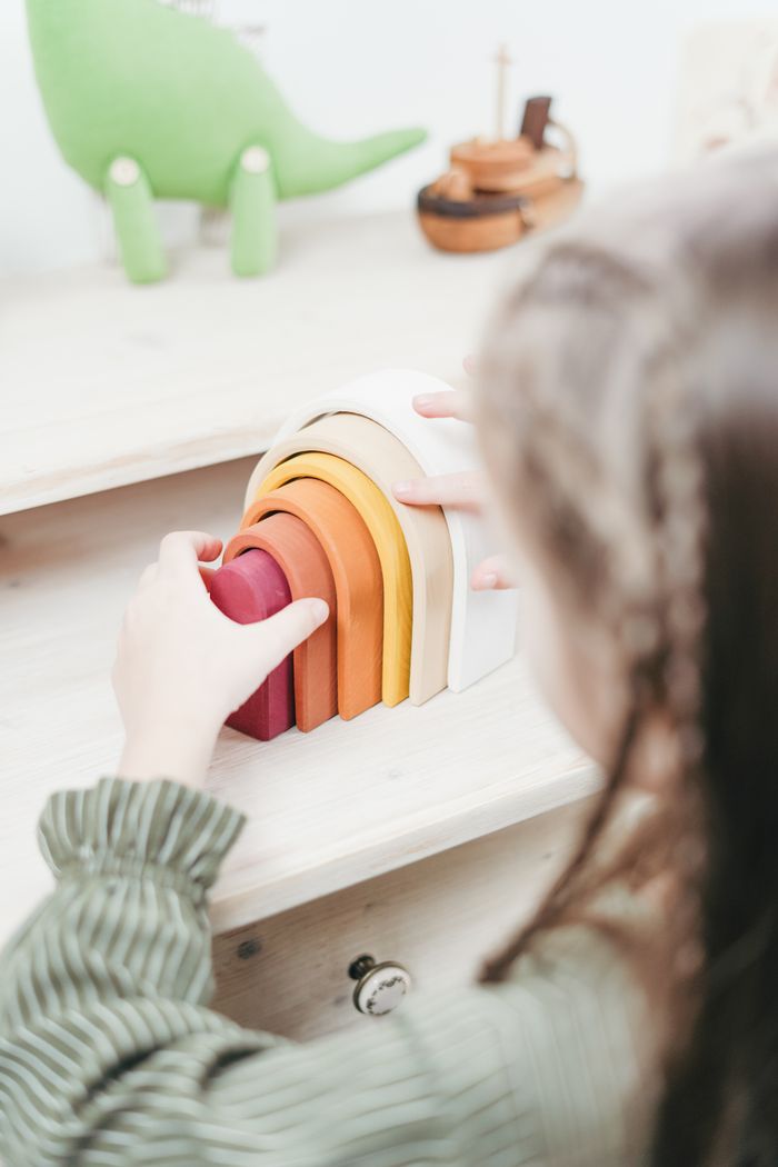Offerings A child engaging in creative play with rainbow-colored wooden toys on a desk.