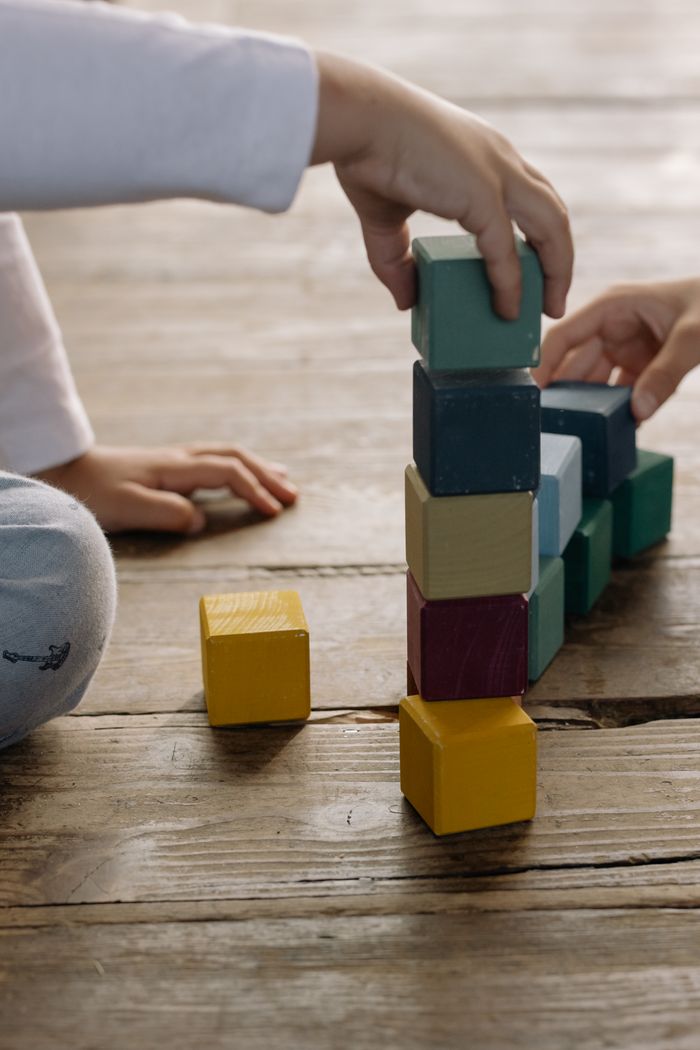 Offerings Kids building a tower with colorful wooden blocks on a wooden floor indoors.