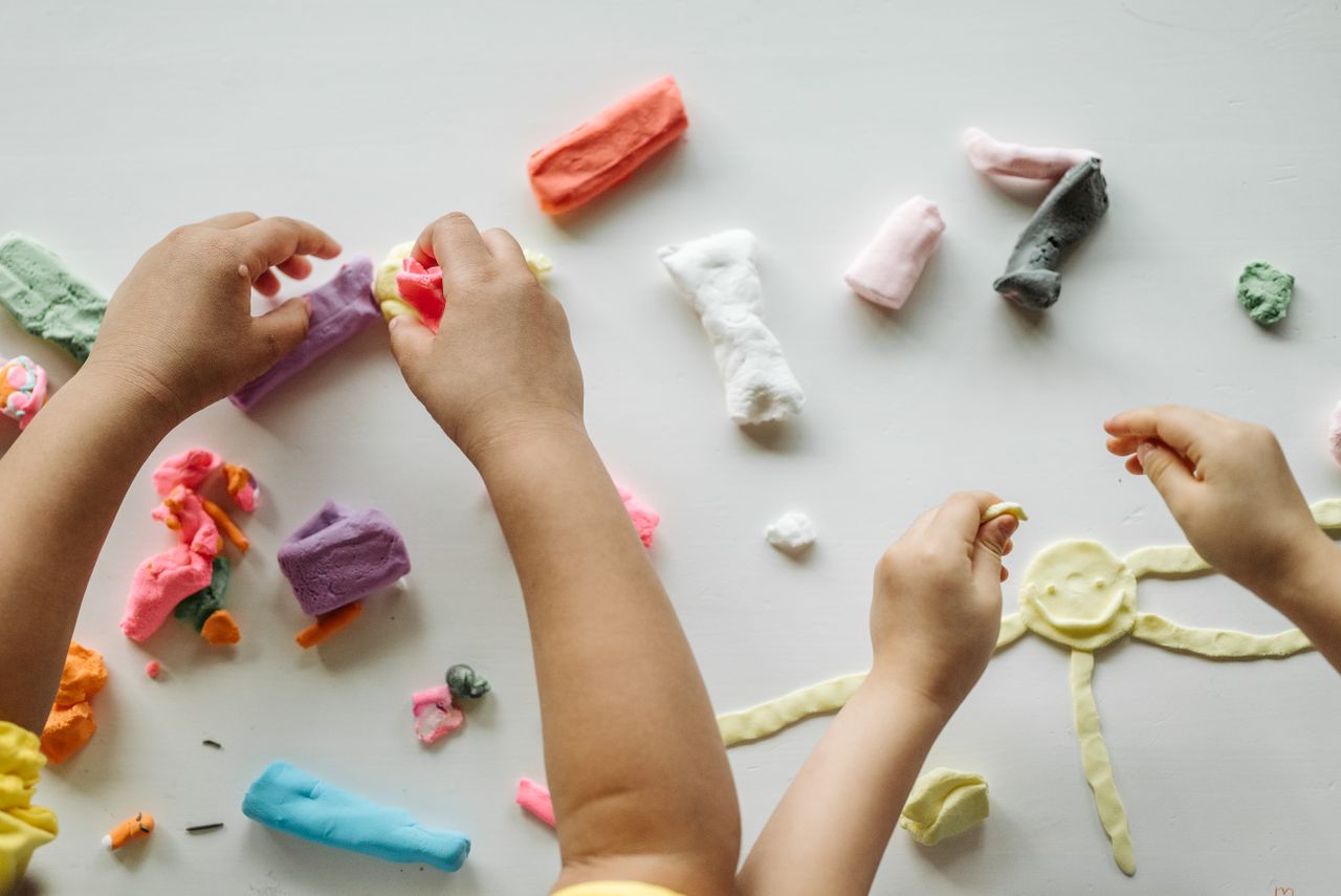 Offerings Children engaged in creative clay play, forming shapes and exploring colors on a white table.